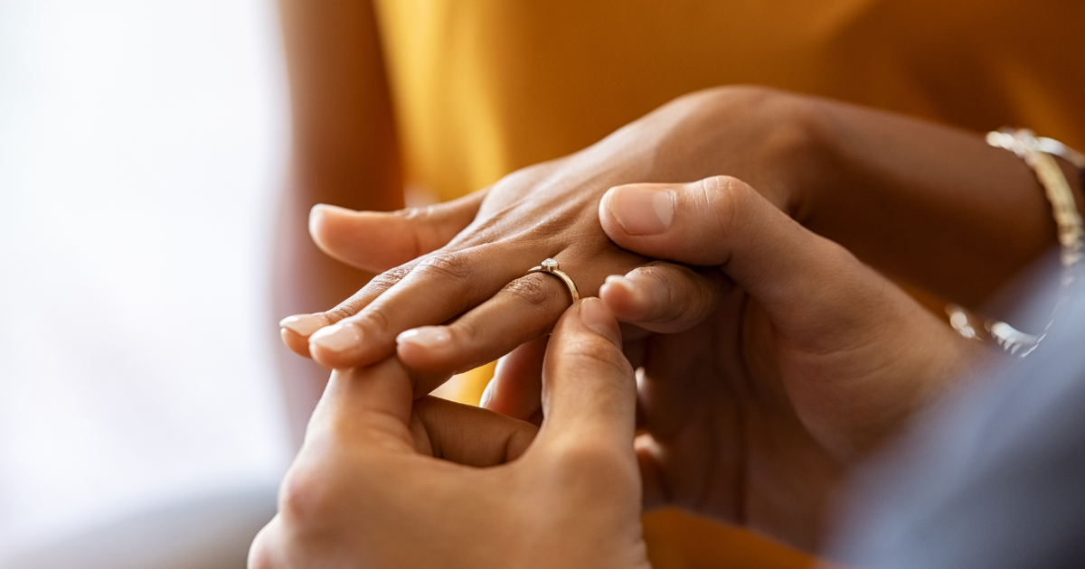 Imagem das mãos de um casal trocando aliança entre eles, aludindo ao casamento